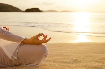 unrecognizable woman meditating at sunset on the beach in the Caribbean